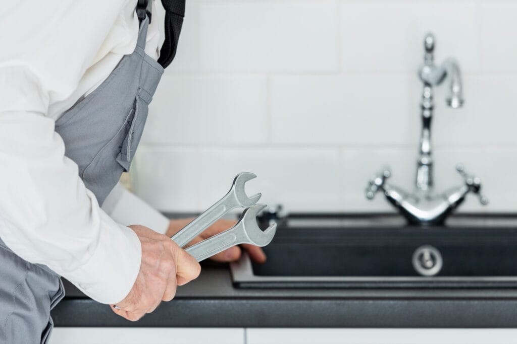 A professional plumber repairing a clogged or leaking kitchen sink with tools in a modern kitchen.