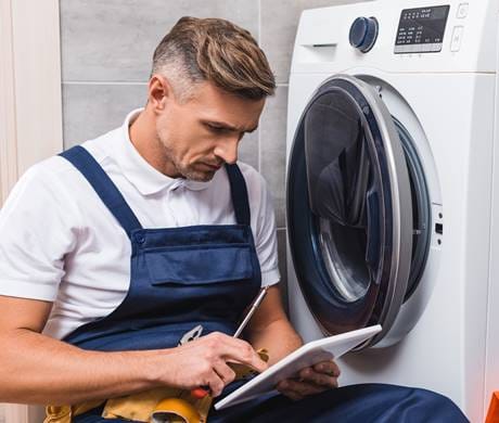 A technician repairing a front-loading washing machine in a modern laundry room.