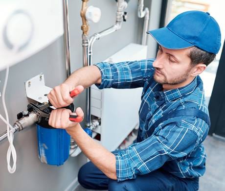 A professional plumber repairing a leaking pipe under a kitchen sink.